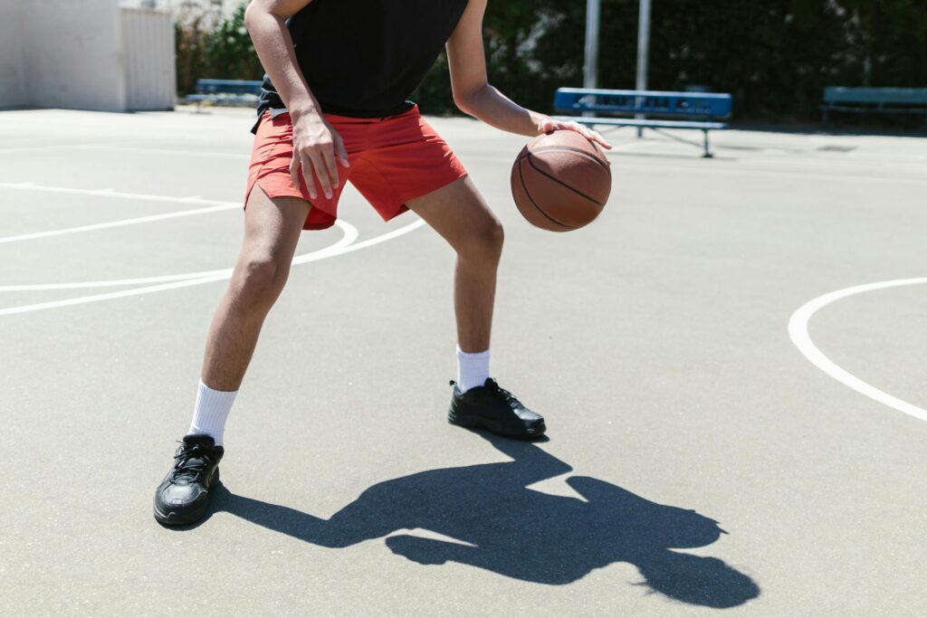 pexels-photo-8337498-8337498 Dynamic shot of an athlete dribbling a basketball on an outdoor court in bright daylight.